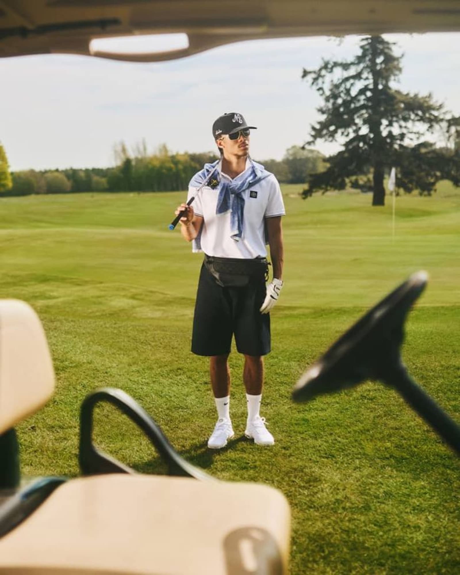 A golfer in a polo and shorts on the course, seen from a cart